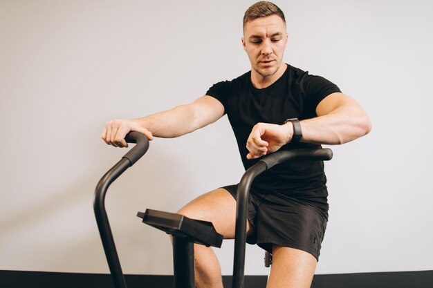 Strong man looking watch and using air bike for cardio workout at cross training gym