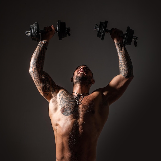 Strong man raising the dumbbells up Intense workout Body with tattoo