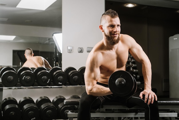 Uomo forte seduto e sollevamento manubri in palestra