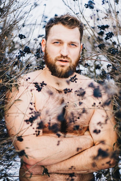 Strong man standing among berry bushes in winter