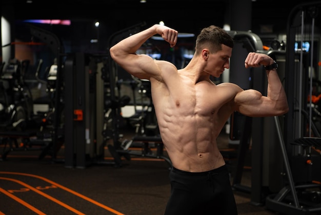 Strong man with fit torso flexing arms muscles standing in double biceps pose in gym strength