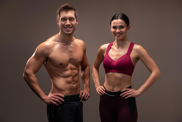 Strong man and woman with well shaped bodies looking at the camera while posing isolated on brown background. Bodybuilding concept