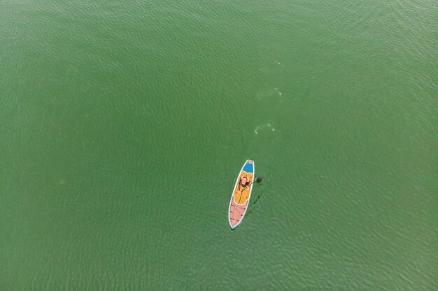 Strong men floating on a SUP boards in a beautiful bay on a sunny day Aerial view of the men crosses the bay using the paddleboard Water sports competitions