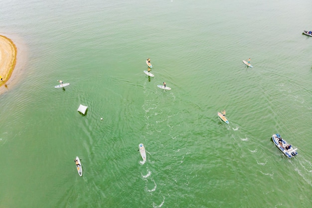 Strong men floating on a SUP boards in a beautiful bay on a sunny day Aerial view of the men crosses the bay using the paddleboard Water sports competitions