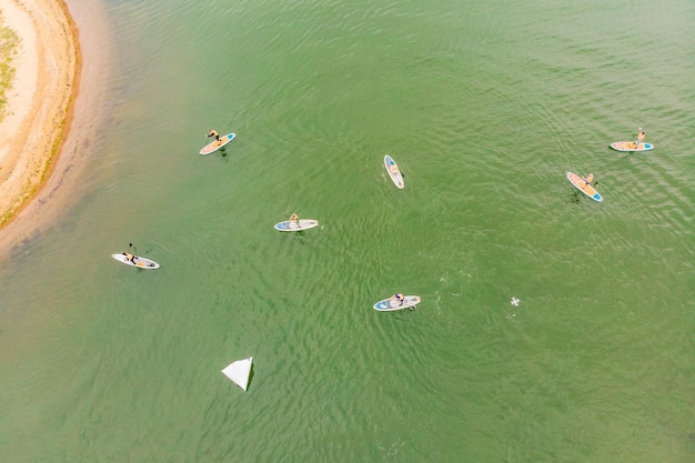 Strong men floating on a SUP boards in a beautiful bay on a sunny day Aerial view of the men crosses the bay using the paddleboard Water sports competitions