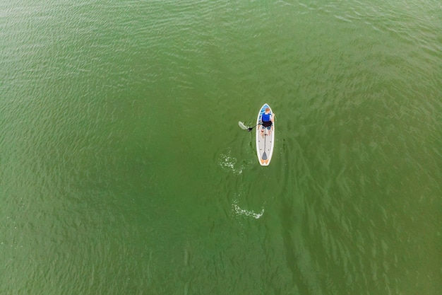 晴れた日に美しい湾のSUPボードに浮かぶ強い男性男性の空中写真は、パドルボードを使用して湾を横断しますウォータースポーツ大会