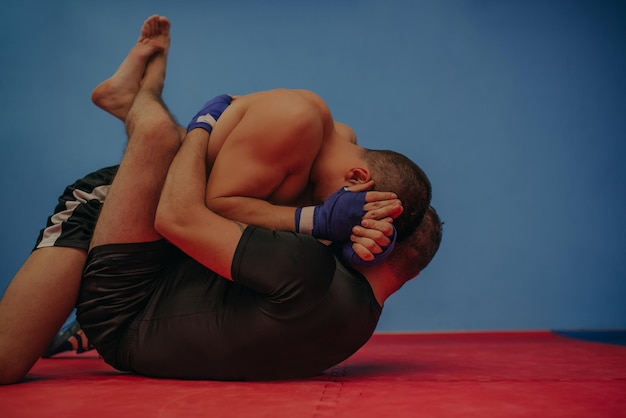 Foto forte combattente di mma che tiene a terra il suo rivale e gli lancia pugni durante un allenamento con molto spazio per la copia