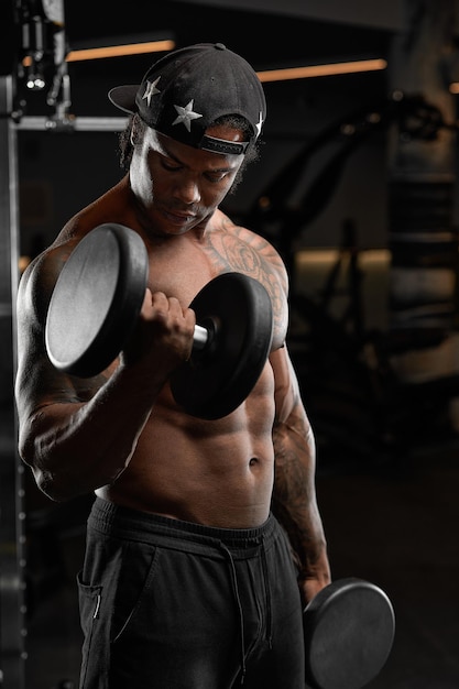 Strong and muscular dark skin man trains on modern equipment in gym Portrait of muscular pumped up fitness trainer