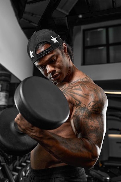 Strong and muscular dark skin man trains on modern equipment in gym Portrait of muscular pumped up fitness trainer