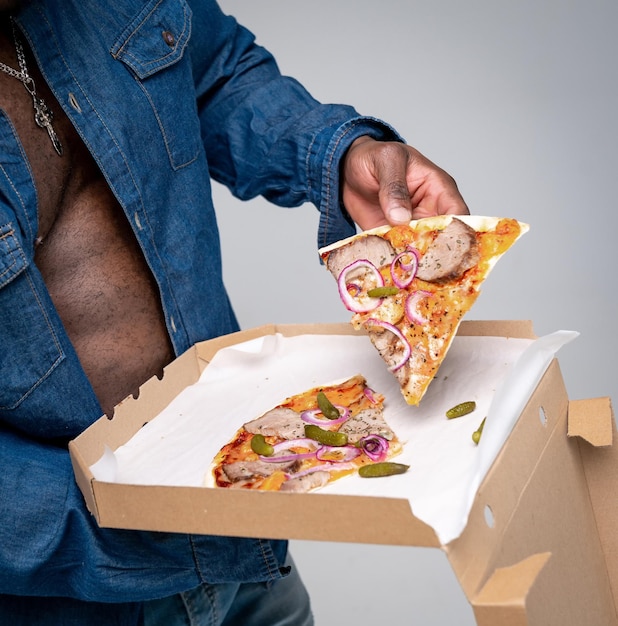 Foto forti mani muscolose tengono la pizza in mano. foto ritagliata selettiva di un afroamericano irriconoscibile affamato con pizza in una scatola. avvicinamento.