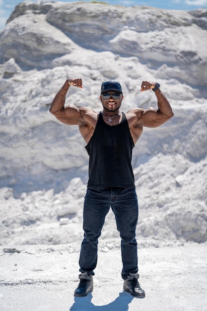 Сильный мускулистый мужчина демонстрирует силу на открытом воздухе Молодой культурист с сильными мышцами
