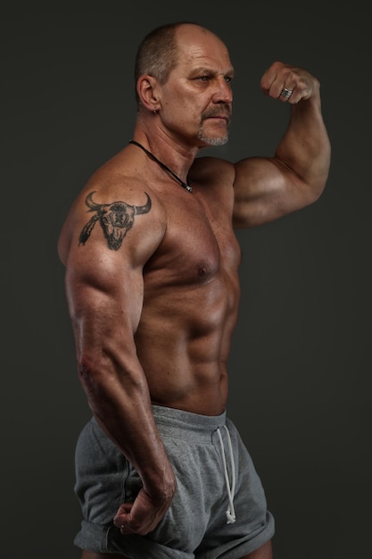 Strong muscular middle age man posing in studio. Isolated on grey.