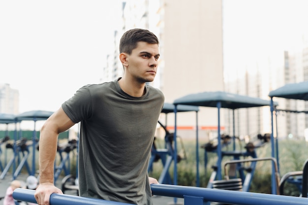 Strong muscular young man is working out in gym outdoor