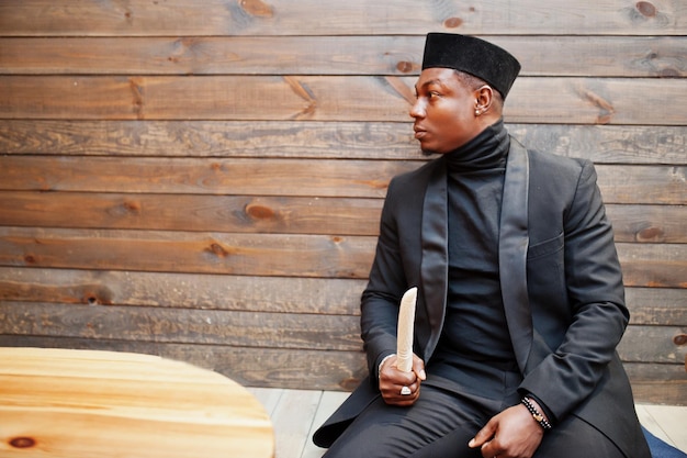 Strong powerful african american man in black suit and turtleneck and cap with elephant tusk