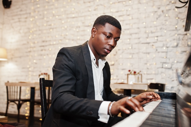 Strong powerful man in black suit play piano