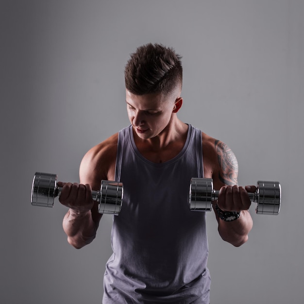 Strong powerful sporty man with muscular healthy body with\
metal dumbbells workout and trains in studio on a gray\
background