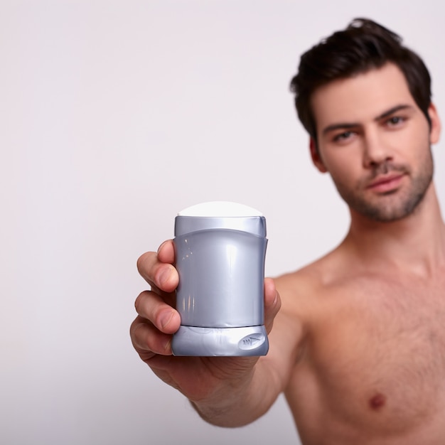 Strong sexy man holds deodorant at white