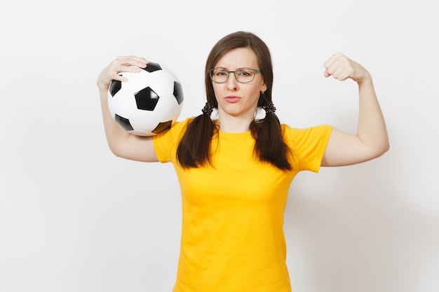 Strong slim european woman, two fun pony tails, football fan or\
player in glasses, yellow uniform hold classic soccer ball isolated\
on white background. sport play football, healthy lifestyle\
concept.