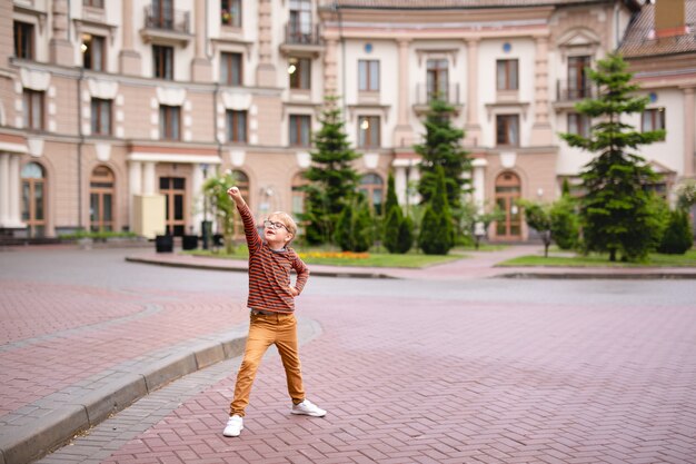 Strong, smart and funny little boy playing outdoors, wearing eyeglasses. 