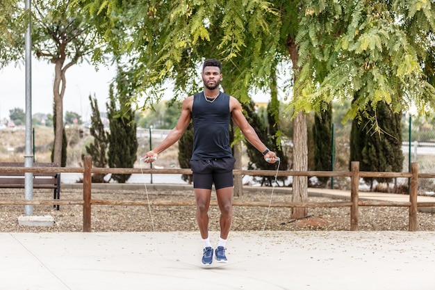 Strong sportsman jumping rope against green trees