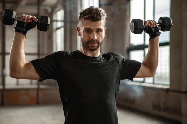 Strong sportsman working out with dumbbells in gym