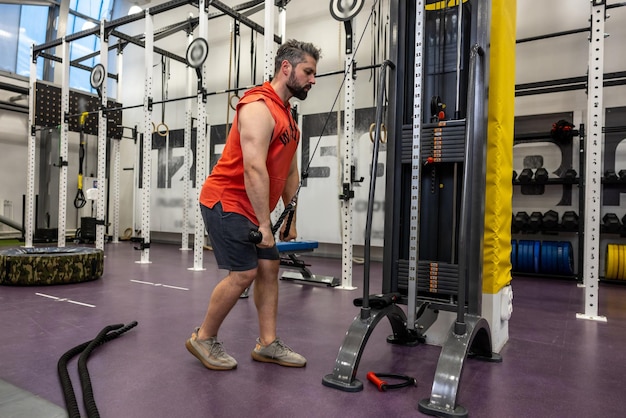 Strong sporty man in sportswear training triceps and biceps at gym doing cable rope pushdowns