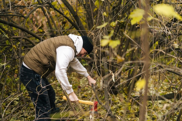 Strong tourist male wearing warm clothes chopping firewood with\
axe in forest on overcast cold day. concept of bushcraft, camping\
and survival in nature.