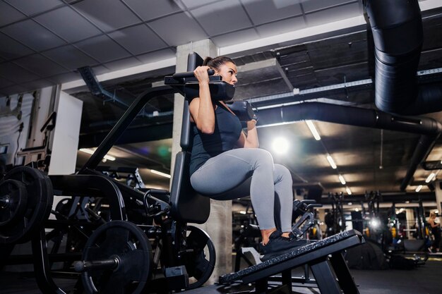 A strong woman is doing exercises for legs and shoulders on a workout machine in a gym