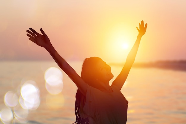 Strong woman raising her hands on sunset background