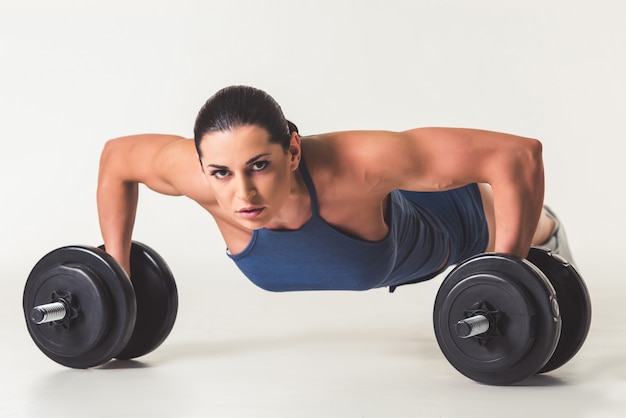 Strong woman in sportswear is working out with dumbbells