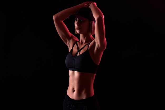 Сильная женщина в спортивном бюстгальтере с мускулистым животом на черном фоне идеальной формы тела