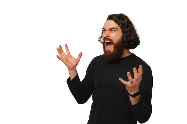 Strong young bearded man with long hair is screaming loud in a white studio