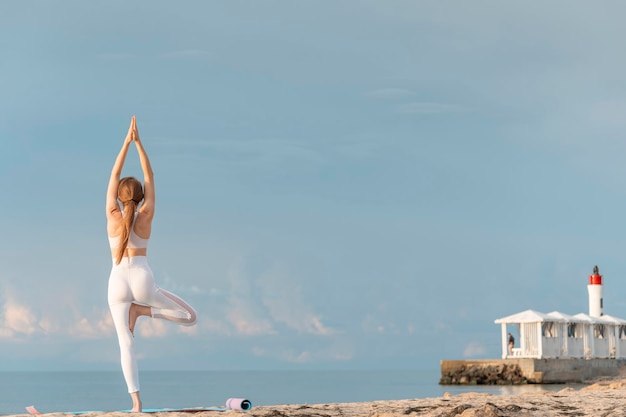 海の背景に屋外でヨガの木のポーズを練習している強い若いフィットネス女性背面図ビーチでヨガ