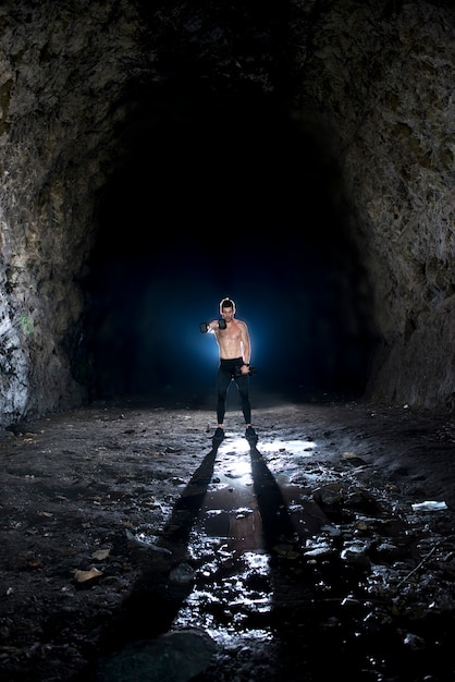 Фото Сильный молодой мужчина, поднимающий гантели в пещере