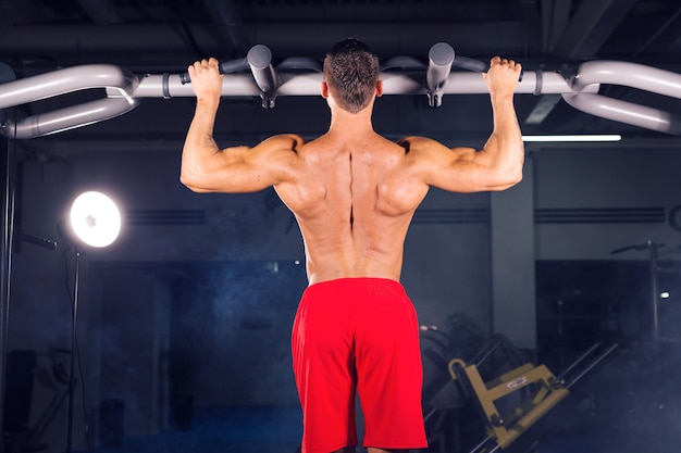 Strong young man doing pull up exercise on horizontal bar in gym