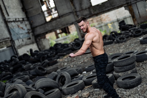 Strong young man lifts tires shirtless Big muscles and perfect abs Many tires on the background Strongman has workout