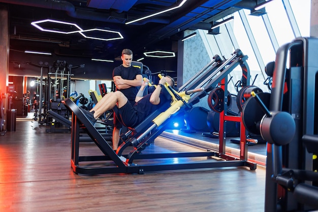 A strong young man performs exercises in the gym under the supervision of a trainer. Powerful workout by a handsome man. Healthy lifestyle