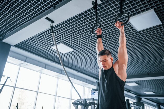 Photo strong young man in sportive clothes doing exercises on gymnastic rings in the gym