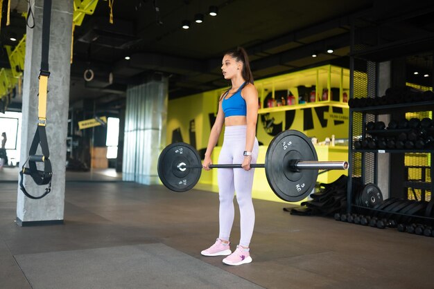 Strong young woman doing situps with a barbell