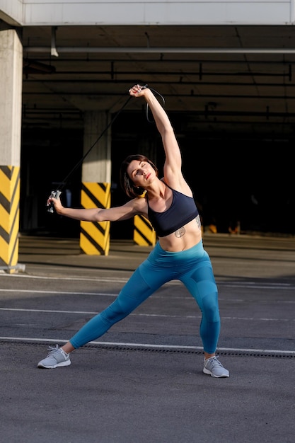 Strong young woman stretching with skipping. Fitness female athlete exercising outdoors.