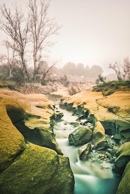 Stroom van zijdeachtig water tussen rotsen op een mistige winterochtend.