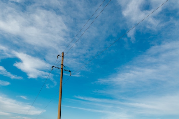 Stroomlijnpost met elektriciteitskabels tegen een heldere hemel met witte wolken, elektriciteitstransmissielijn, voeding