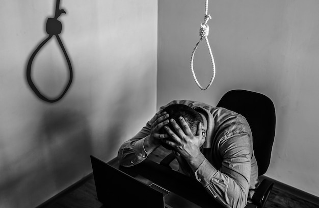 Strop is boven de kantoormedewerker. Zelfmoordconcept. Opknoping vanwege werkstress. Depressie van burn-out. Vreselijke levenssituatie. Man in de buurt van de laptop aan de balie.