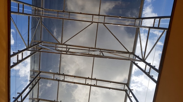 정면의 구조용 유약. 현대적인 건물에 유리 천장 요소가 있는 추상적인 배경. 격자 요소로 구분된 유리창을 통해 푸른 하늘의 전망.