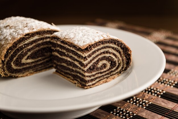 Strudel with poppy seeds on a ceramic white plate on wooden background