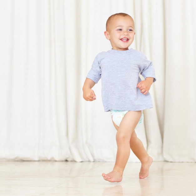 Photo strutting his stuff full length shot of a cute little boy walking around the house in a nappy and tshirt