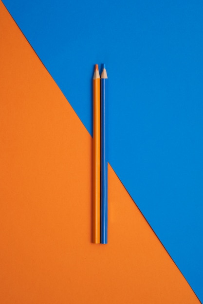 Stuck blue and orange colored pencils isolated on orange and blue table