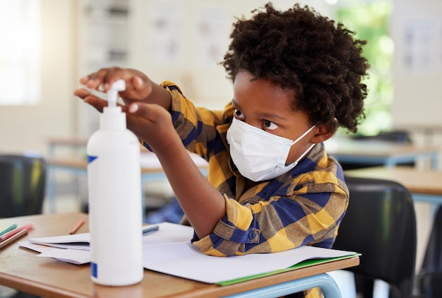 Student applying sanitizer in school class for hygiene clean hands and to protect from spread of covid and cold germ Afro child or little boy learning and getting education in corona virus pandemic