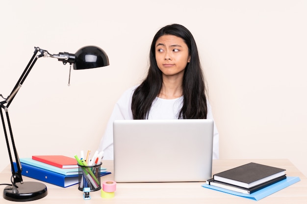 Student asian girl in a workplace with a laptop isolated on beige