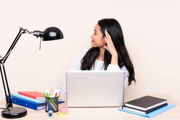 Ragazza asiatica dello studente in un posto di lavoro con un computer portatile isolato su beige